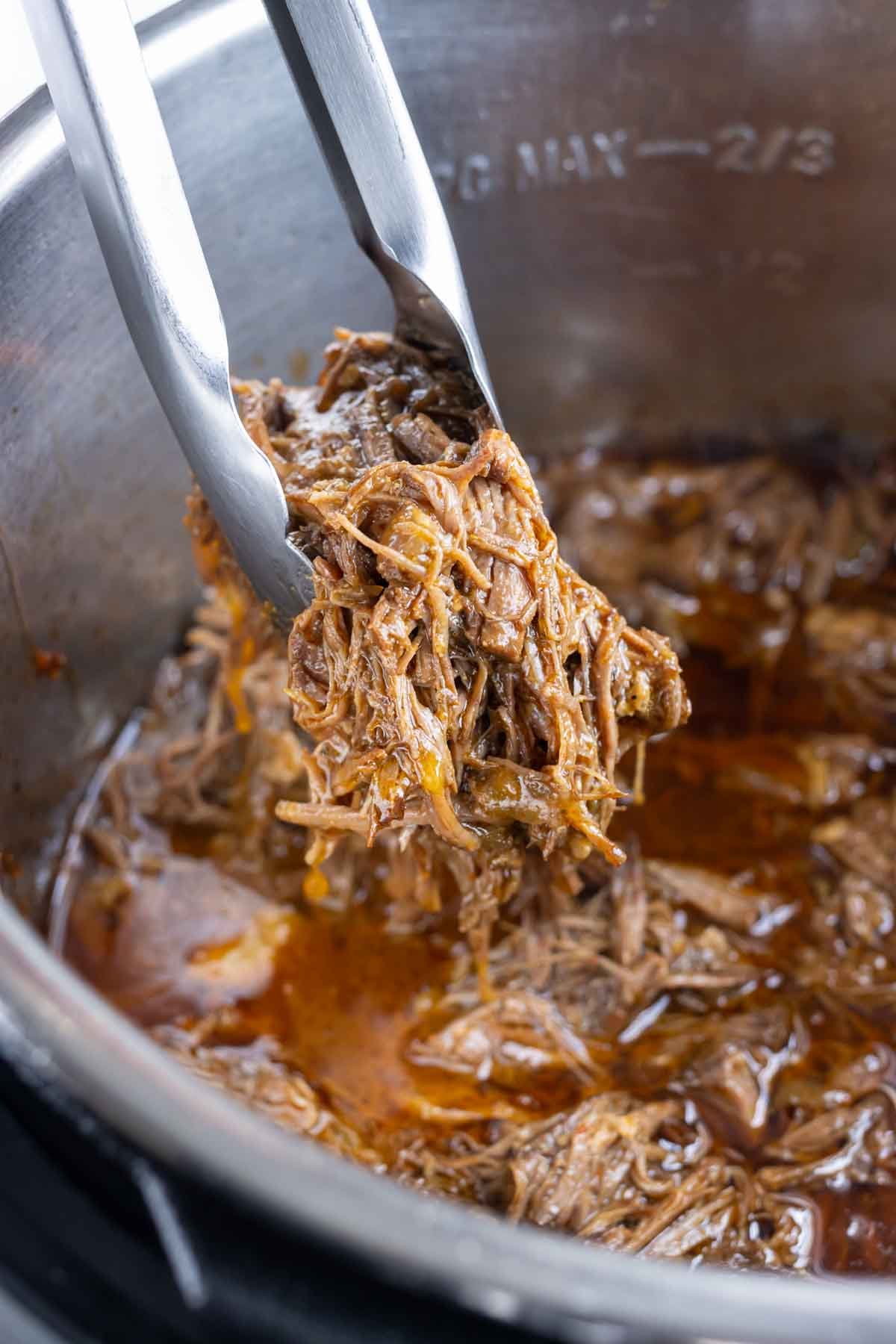 Shredded Mexican beef is removed from the pressure cooker with tongs.