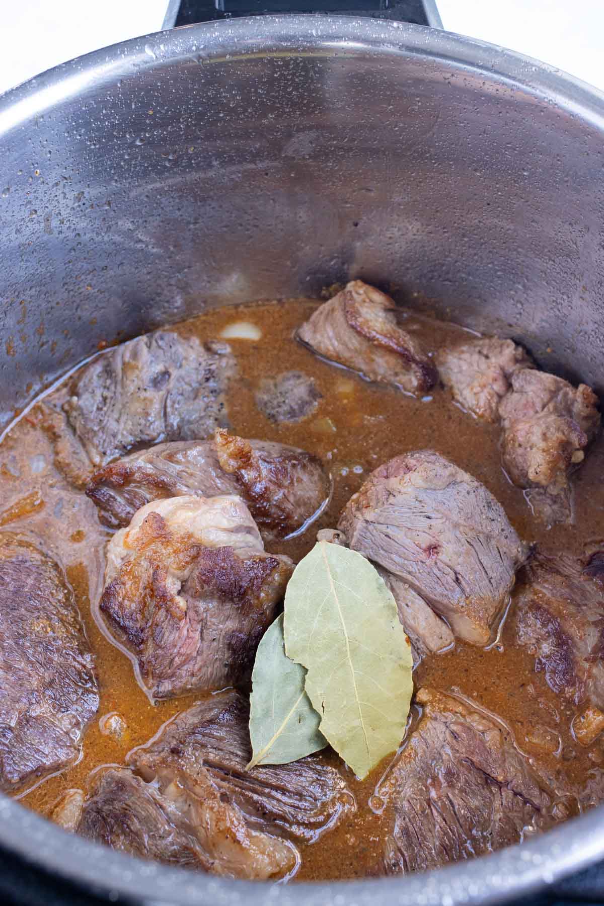 Beef and sauce is added back to the instant pot with bay leaves.