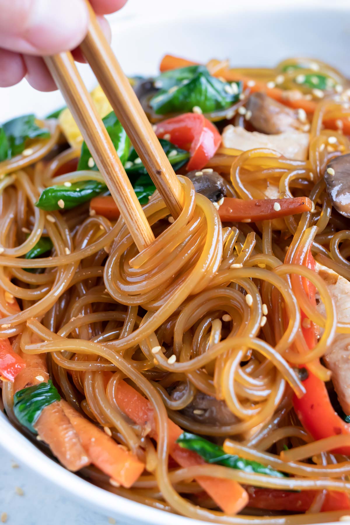 Glass noodles in a Japchae recipe are twirled by chopsticks.