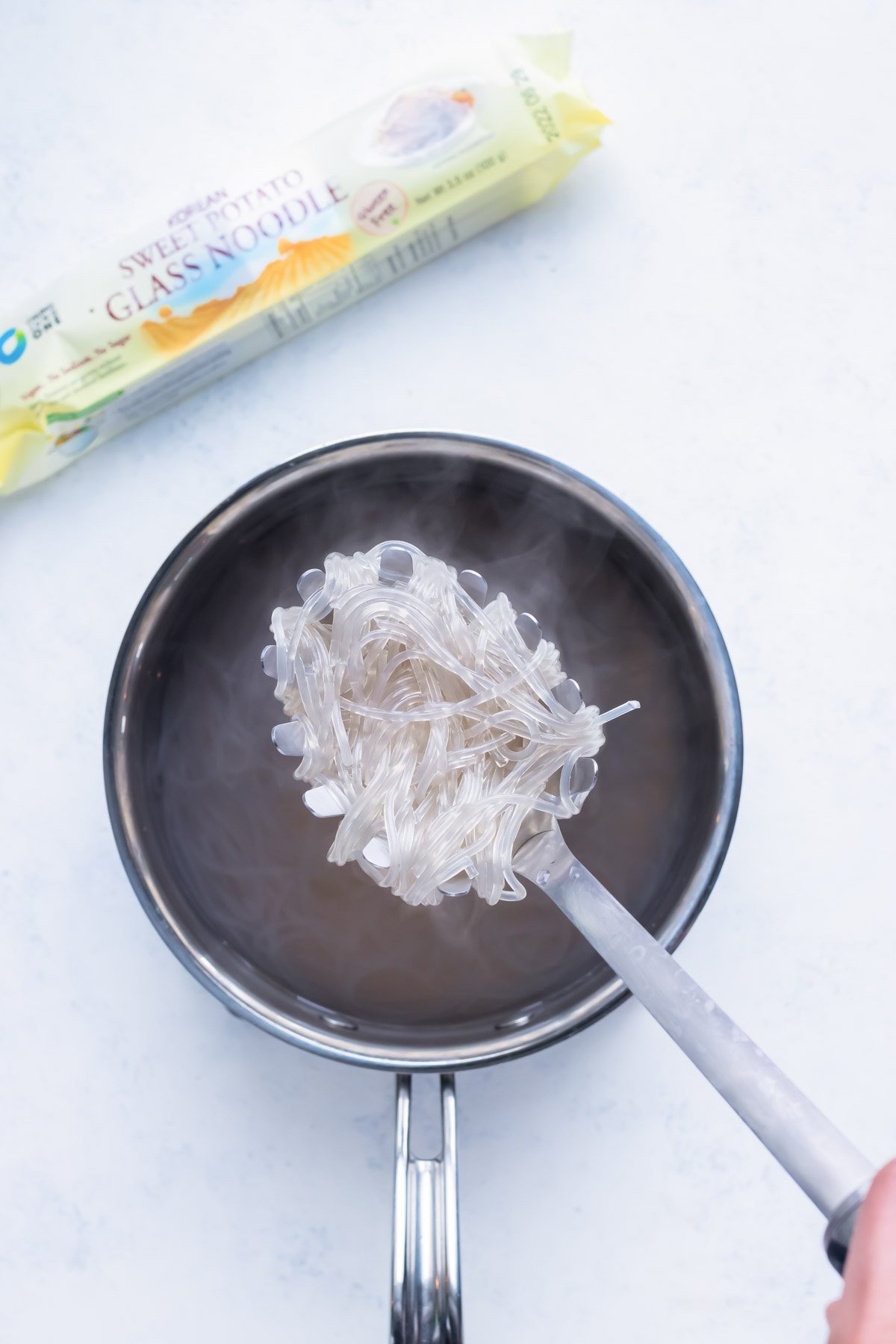 Glass noodles are cooked and lifted out of a pot.