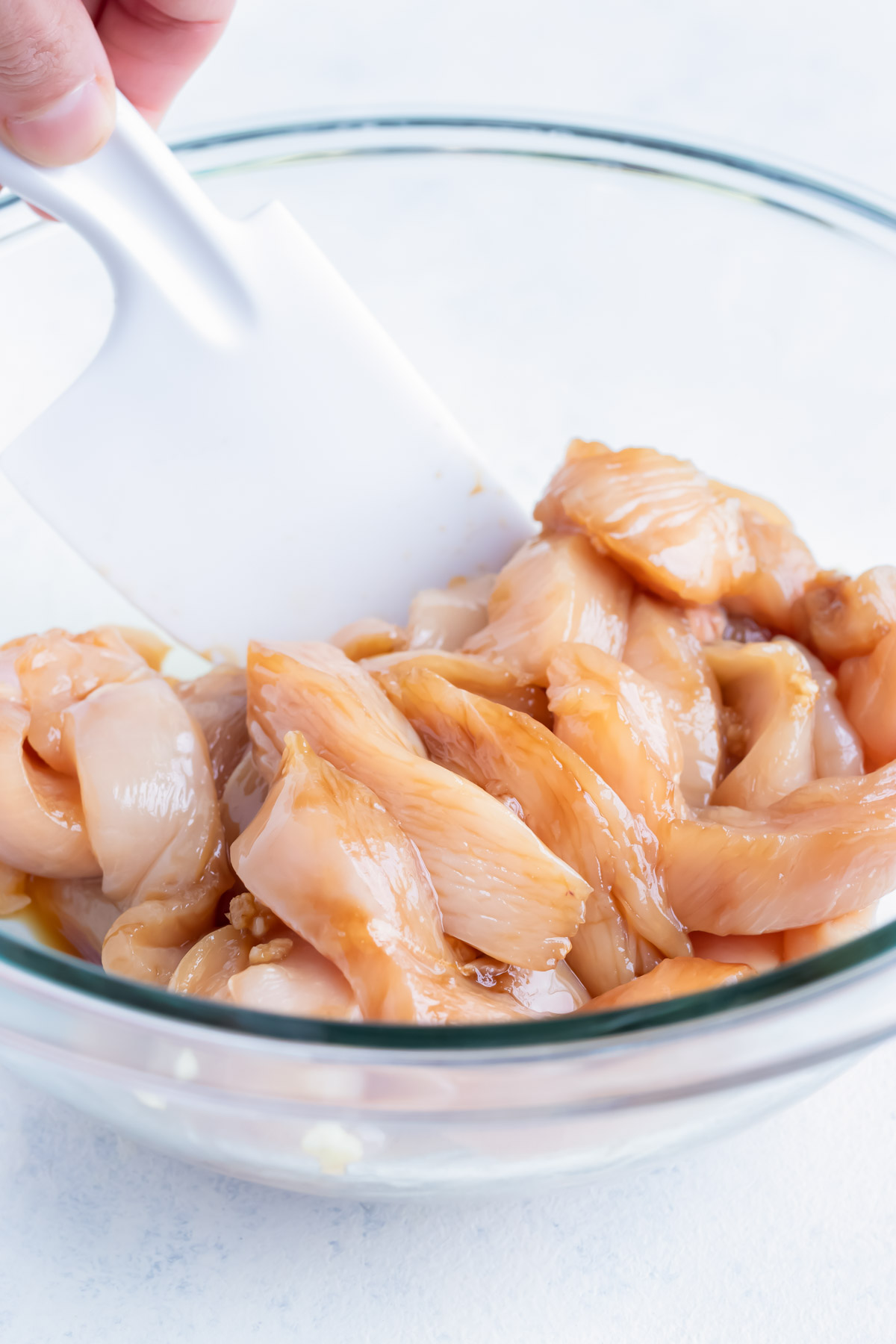 Sliced raw chicken is marinated in a glass bowl before cooking.