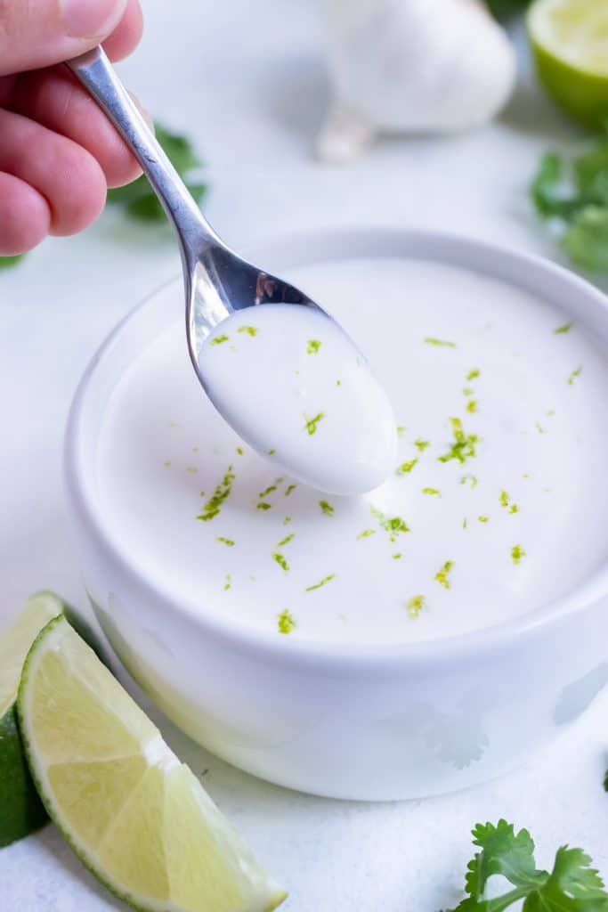 A spoonful of lime crema is being picked up from a bowl to be used as a fish taco sauce.