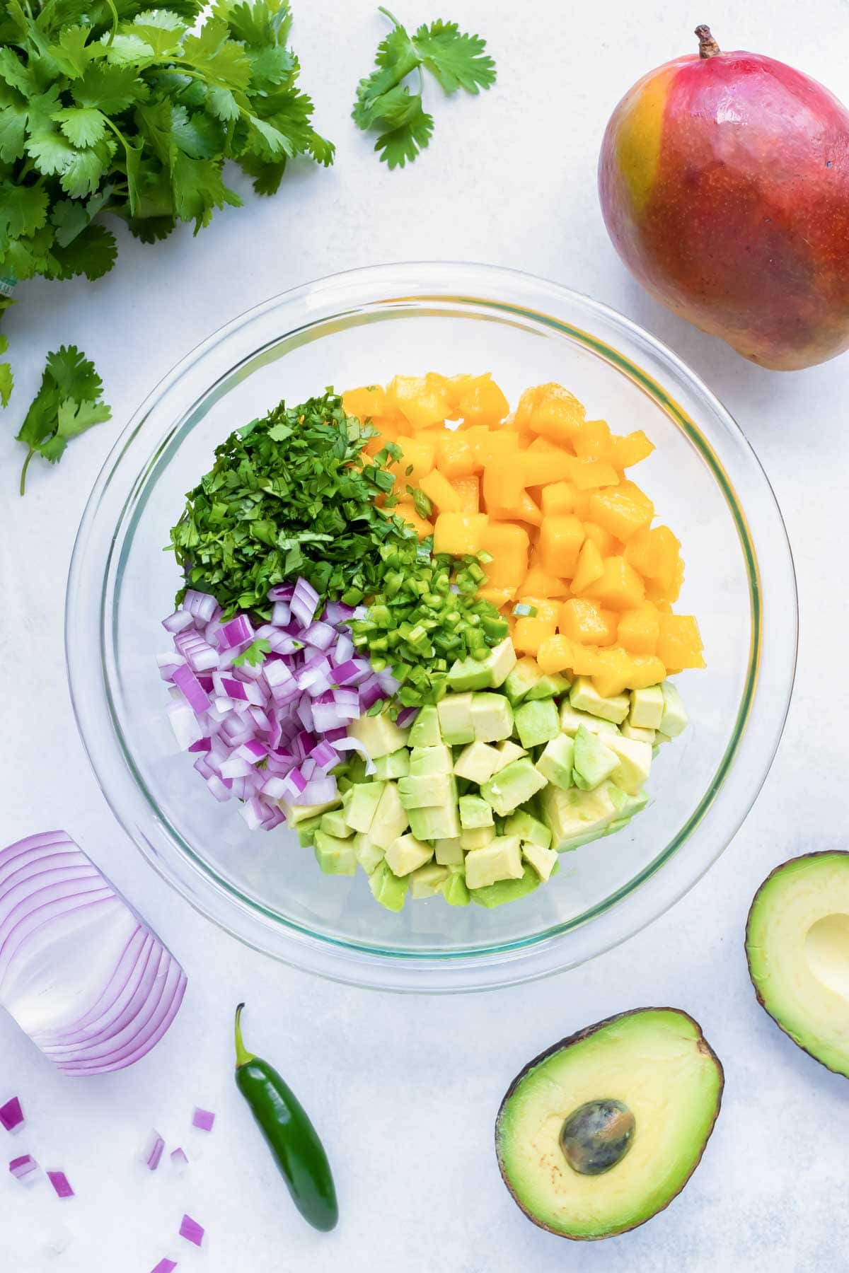 A large bowl full of diced mango, avocado, red onion, cilantro, and jalapeno for a salsa recipe.