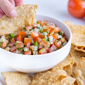 A hand is used to dip a tortilla chip into the fresh pico.