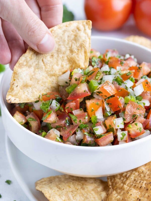 A bowl of pico de gallo is eaten out of by a chip.