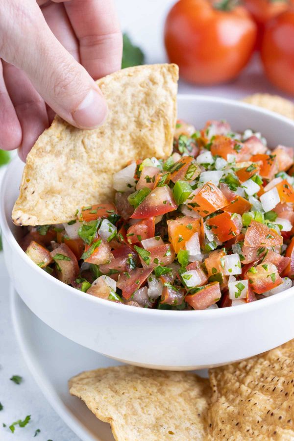A bowl of pico de gallo is eaten out of by a chip.