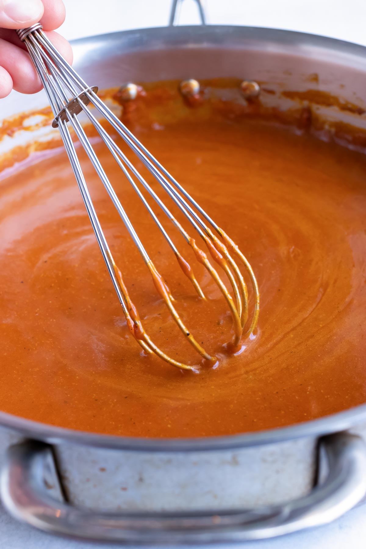 Whisking a red enchilada sauce in a skillet.