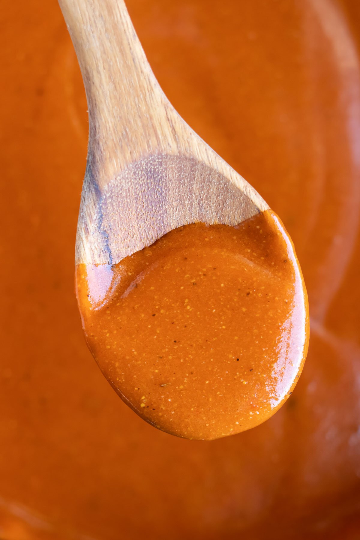 A wooden spoon stirring a red enchilada sauce.