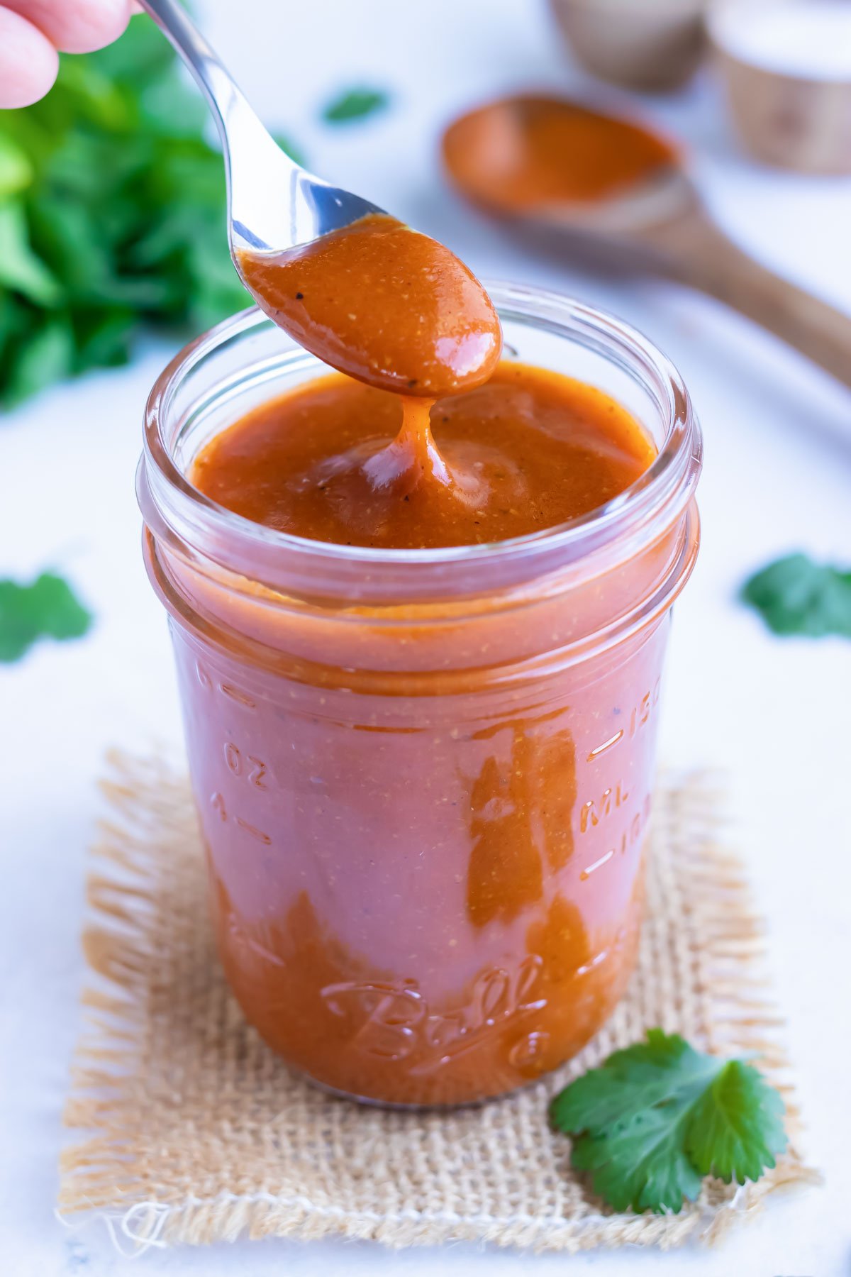 A silver spoon with creamy tomato-based red enchilada sauce sliding off the end of it.