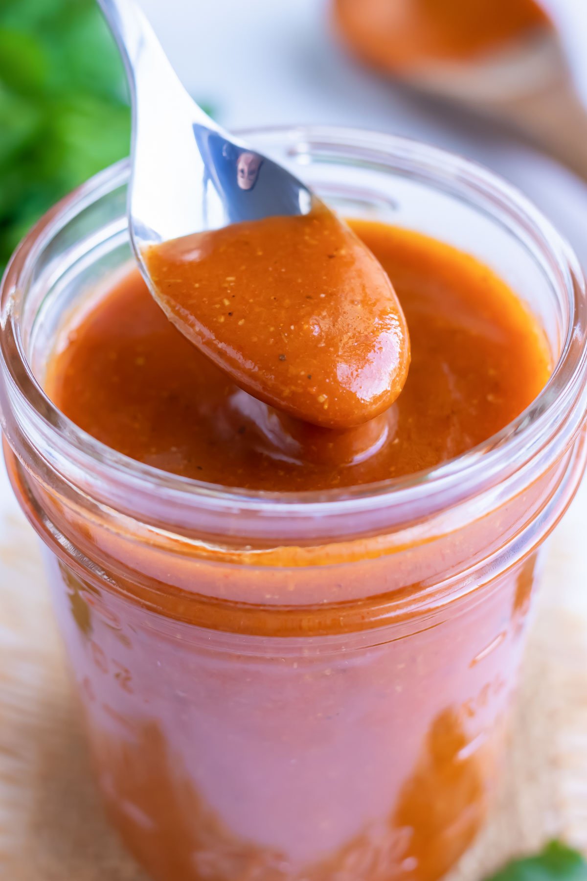 A spoon scooping out some red sauce from a glass storage jar.
