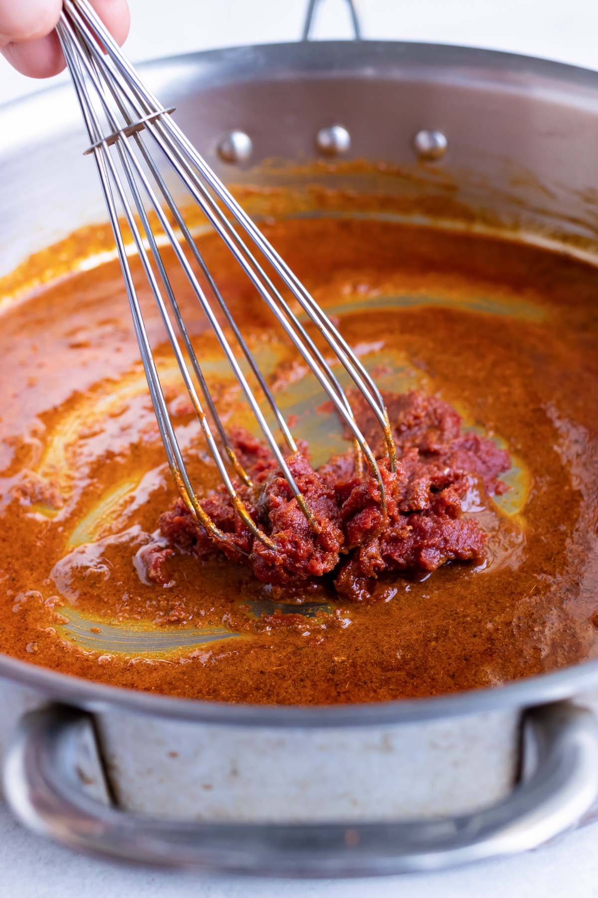 Adding tomato paste to a roux in a large skillet.