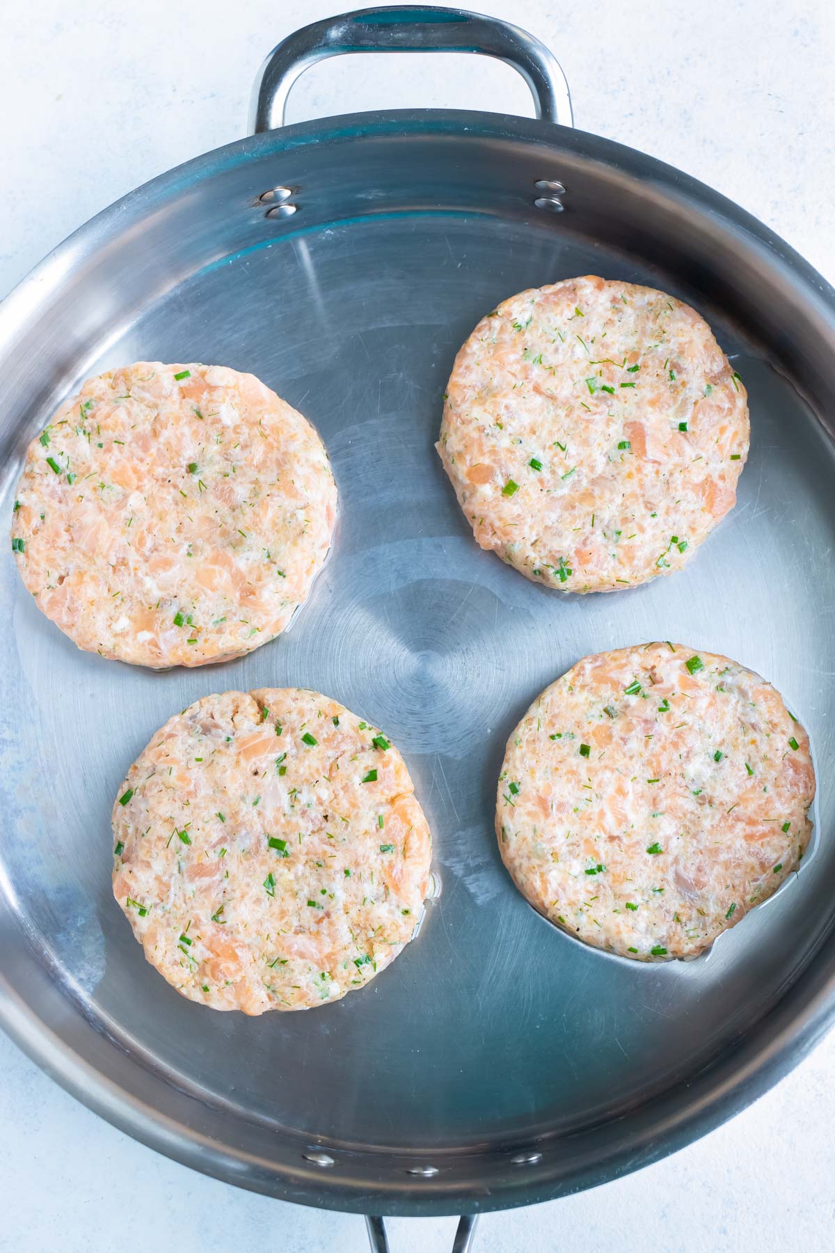 Salmon burgers are cooked in a skillet on the stove.
