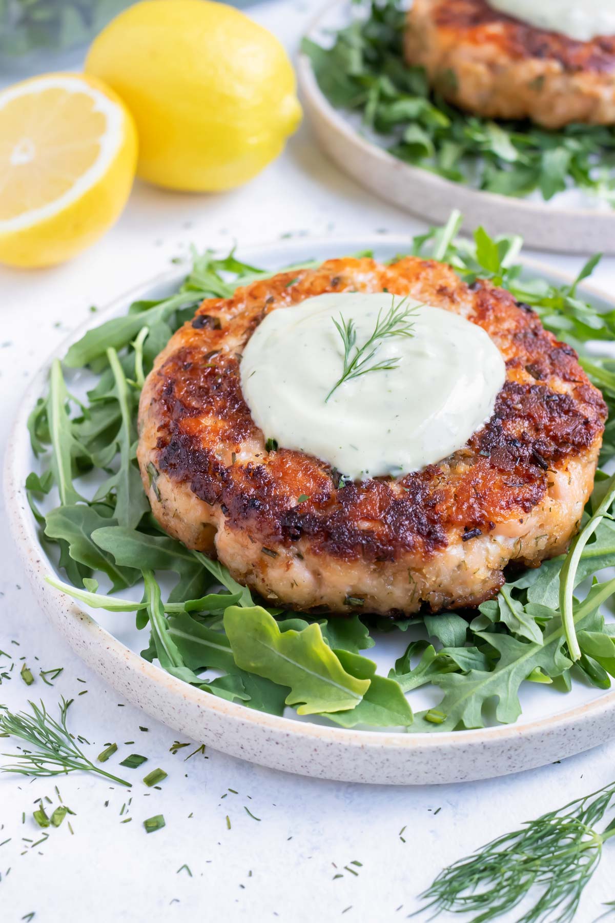 Salmon burger is served on a plate with greens and homemade avocado sauce.