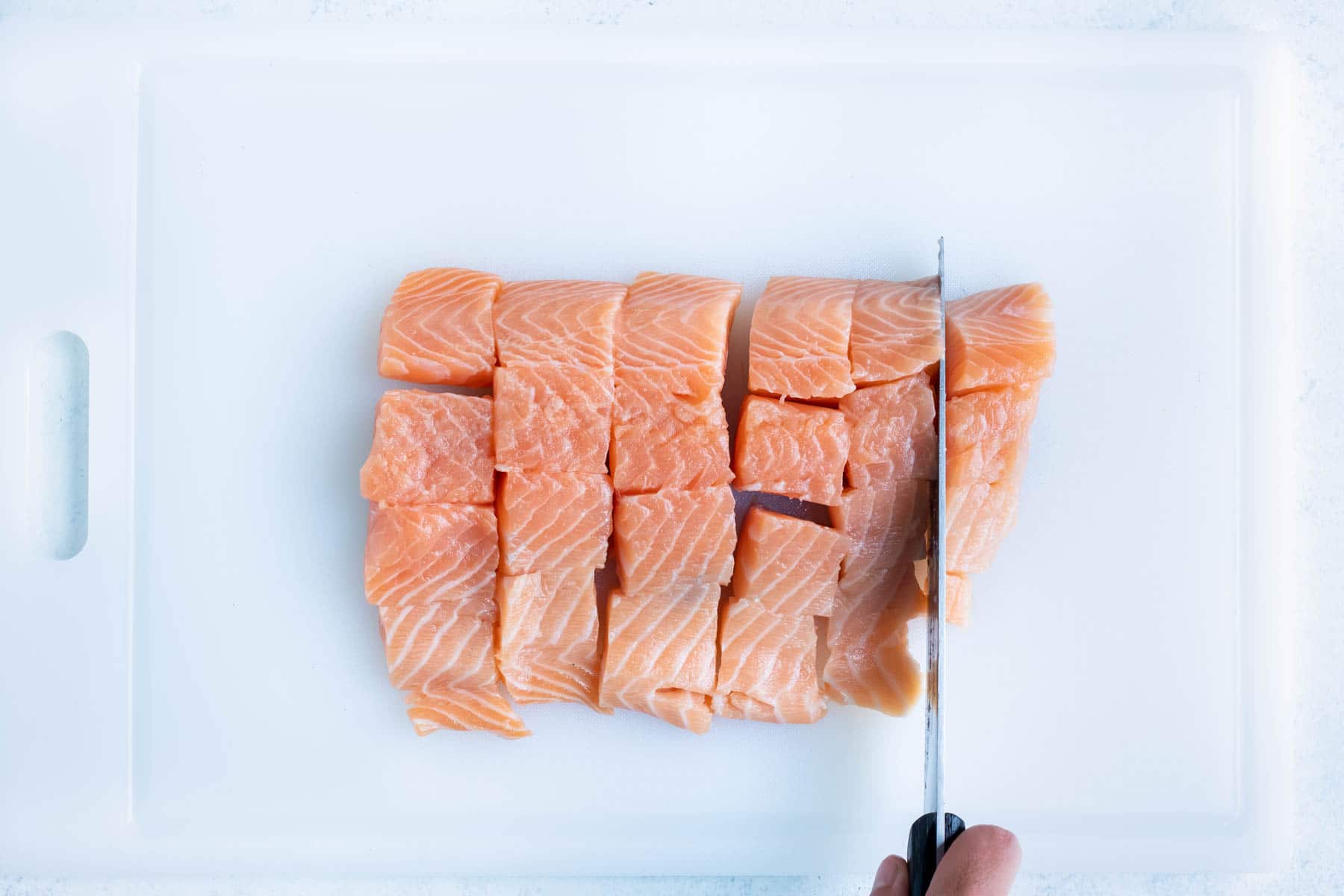The fresh salmon is cubed with a knife.