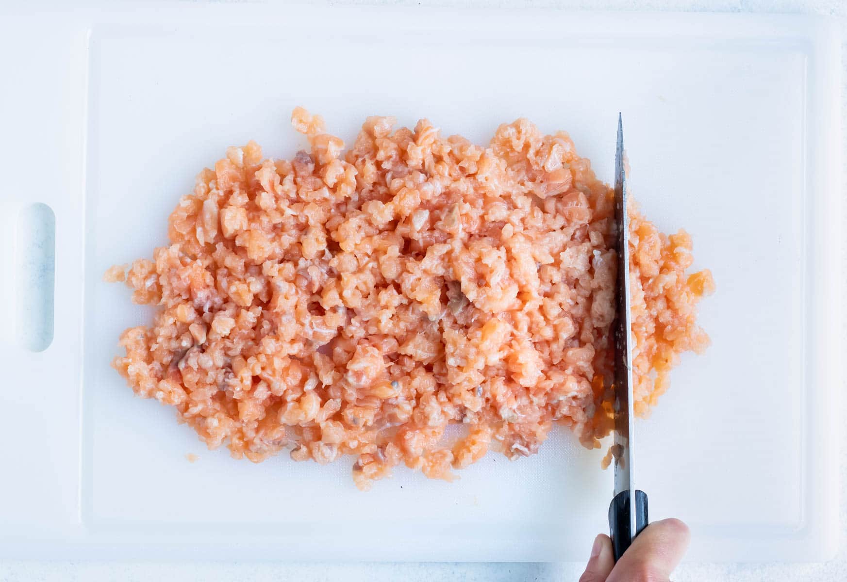 Salmon is chopped finely with a knife on a cutting board.