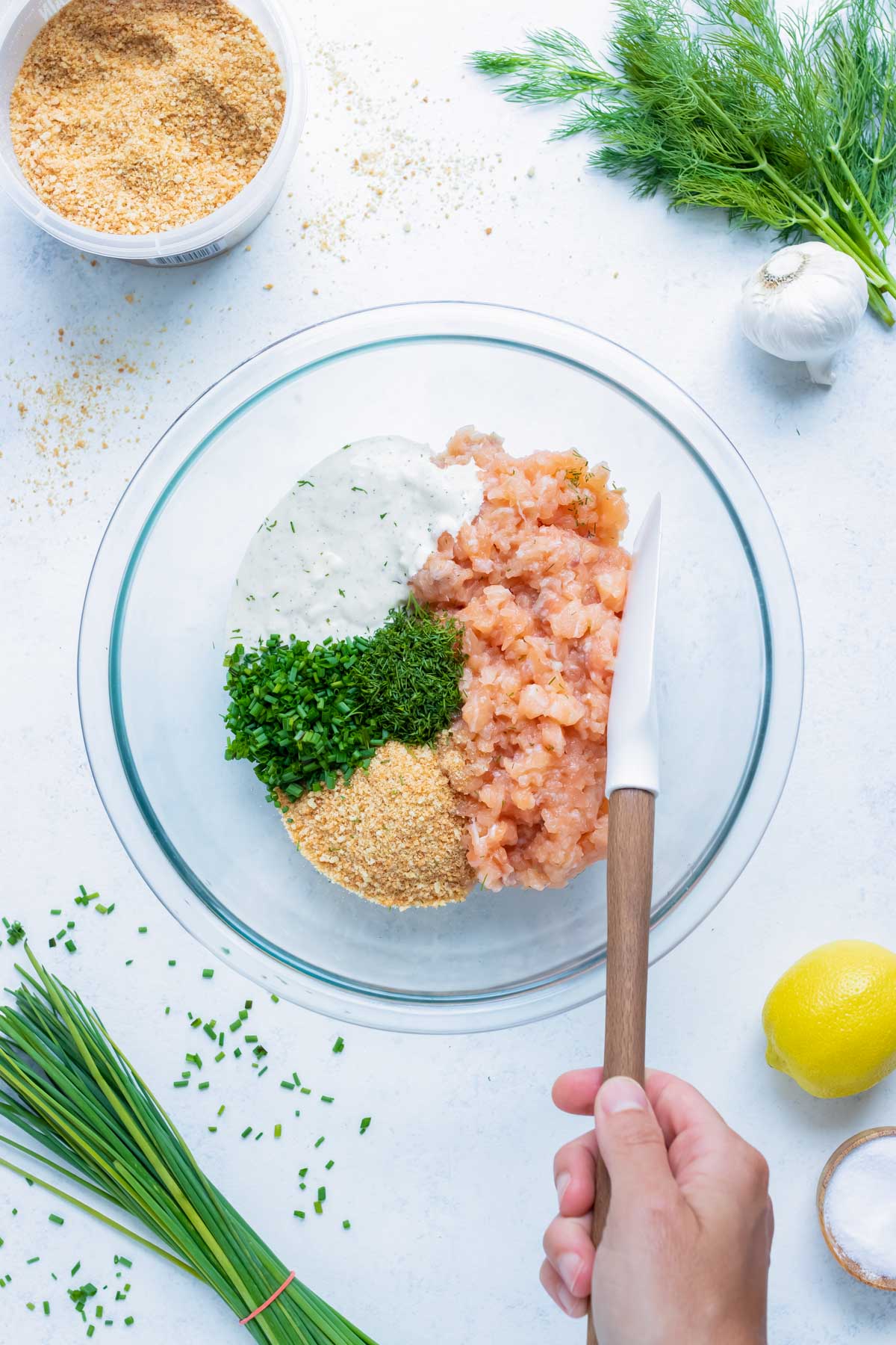 Salmon burger ingredients are combined in a glass bowl.