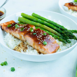 A plate is used to serve a seafood dinner with teriyaki salmon, asparagus, and rice.