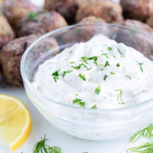 Authentic, vegetarian tzatziki sauce full of dill and cucumber is placed in a glass bowl for dipping meatballs, gyros, or falafel.