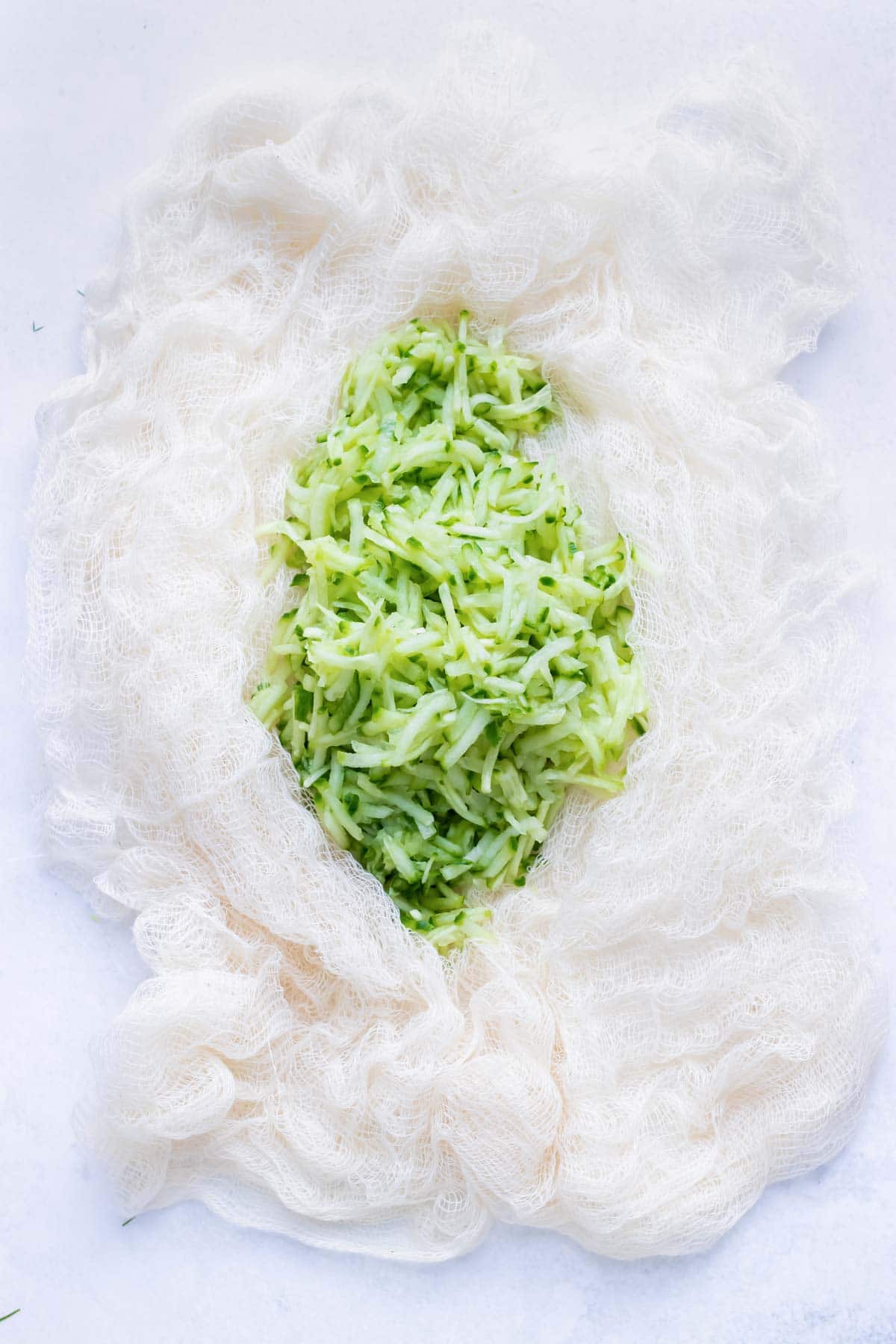 Shredded cucumber is set to rest and placed in a cheese cloth to remove liquid before adding to the food processor in this easy tzatziki sauce.