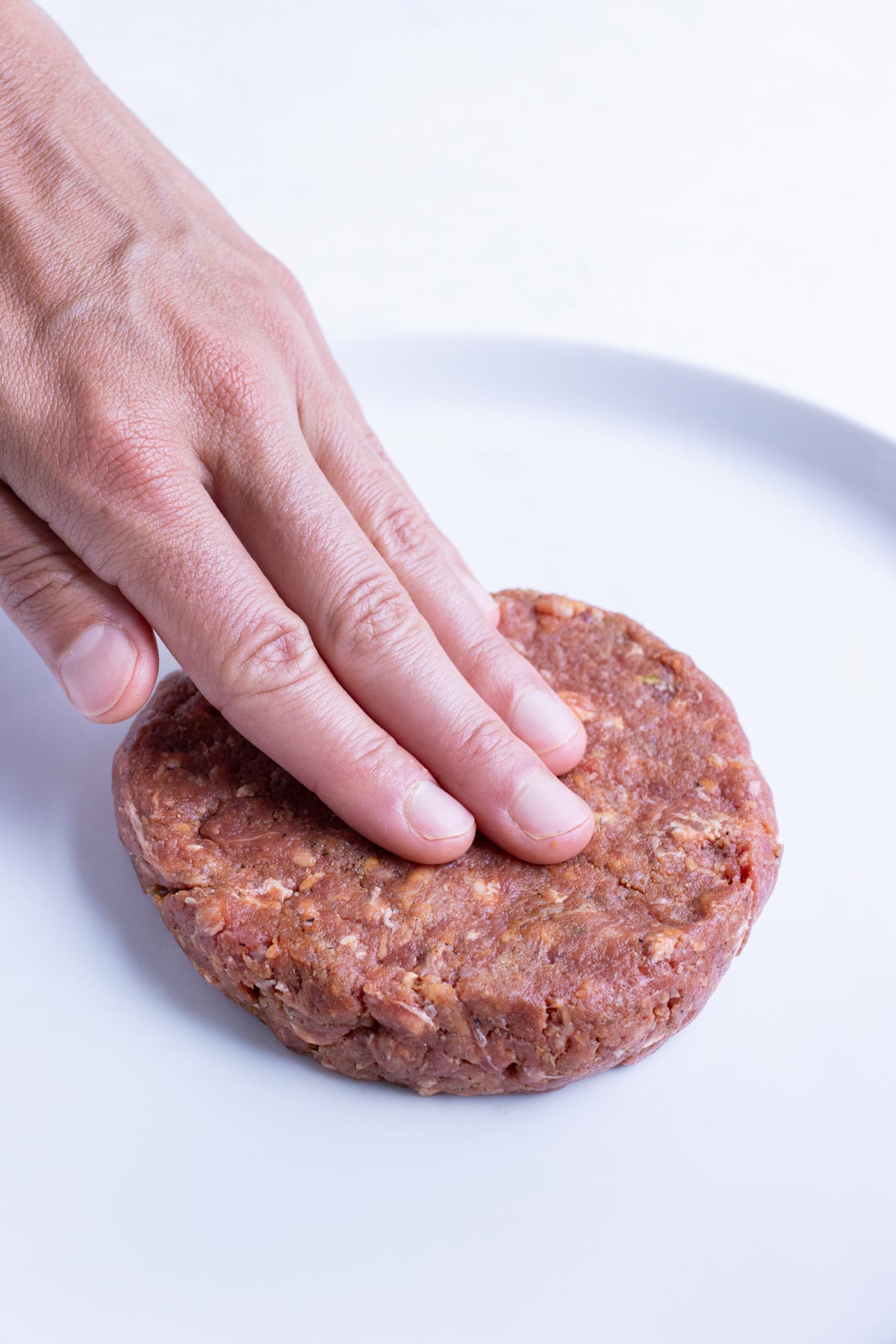 Hands are used to form a hamburger patty.