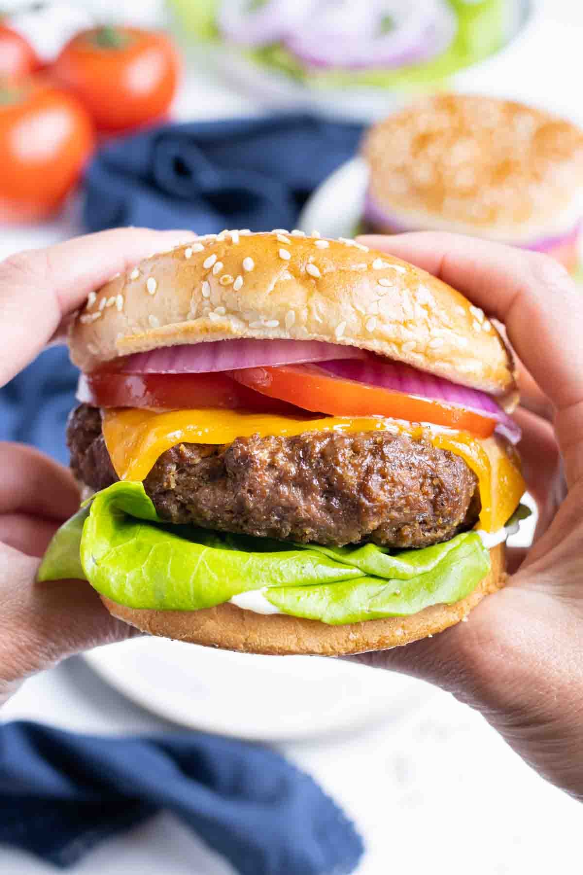 Hands are shown holding a hamburger before eating.