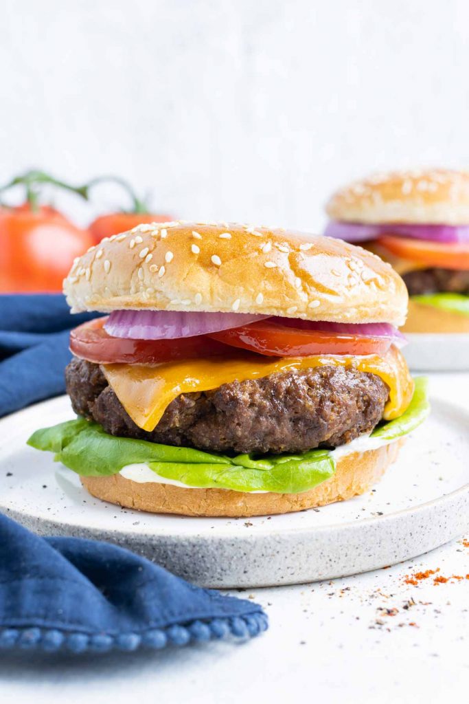 Cheese burgers are topped with lettuce, tomatoes, and red onion.