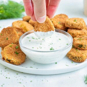 A pickle is dipped into the ranch sauce.