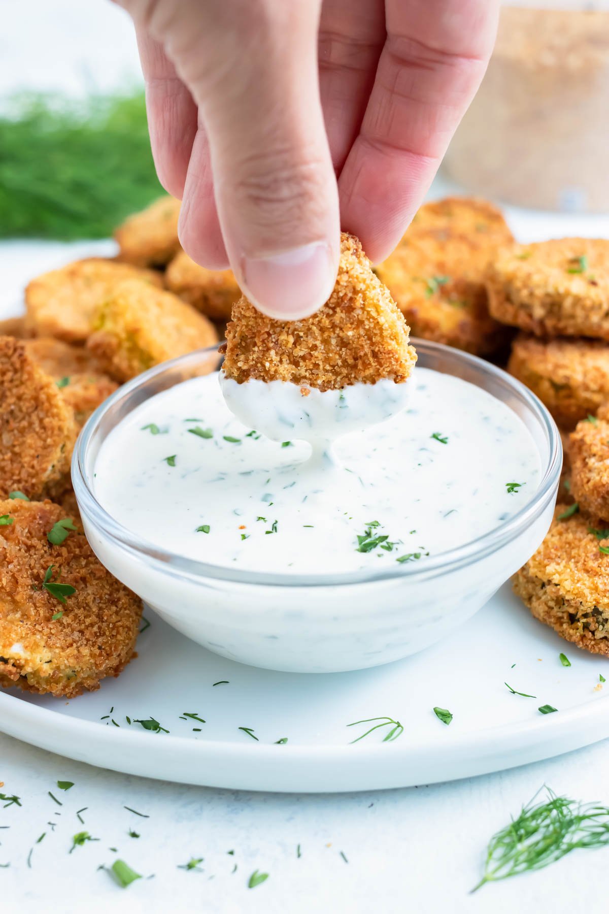 A hand dips a gluten-free air fryer pickle into dip.