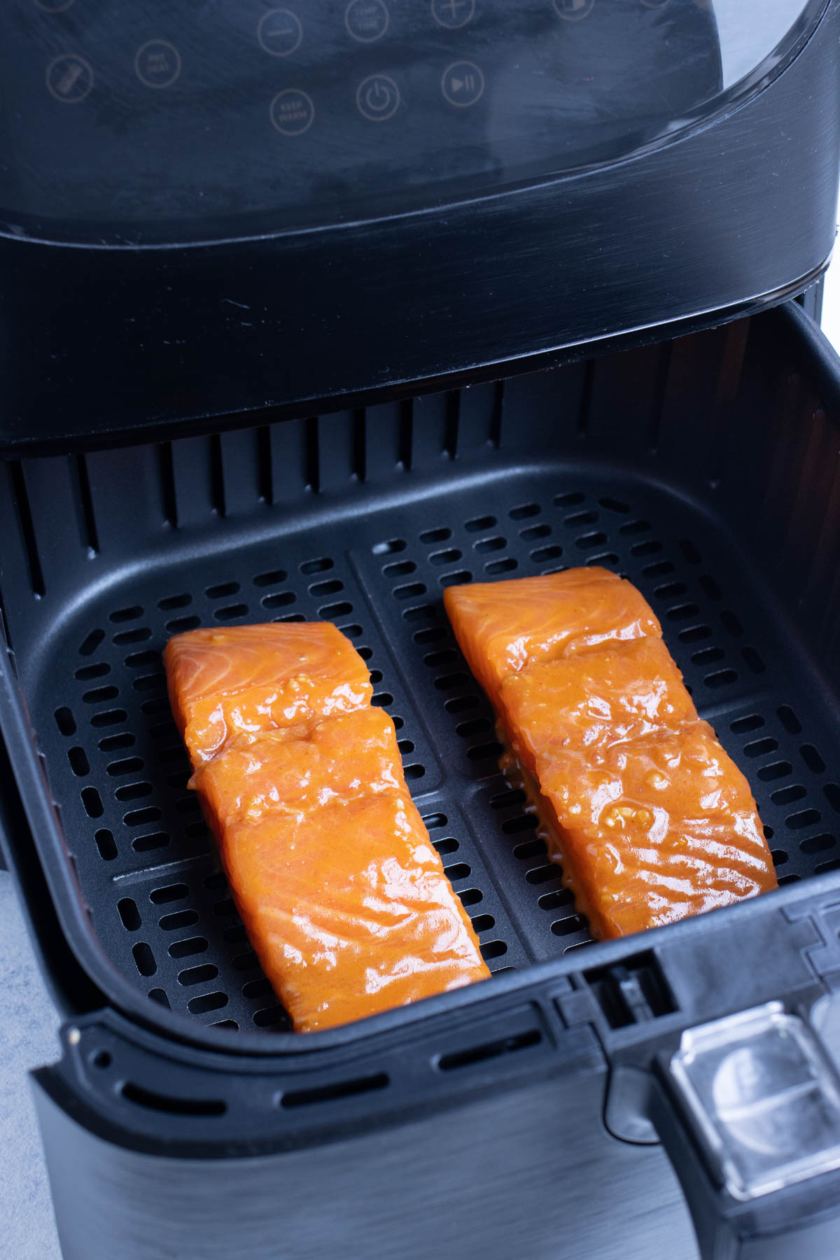 Marinaded salmon is set inside the air fryer skin side down.