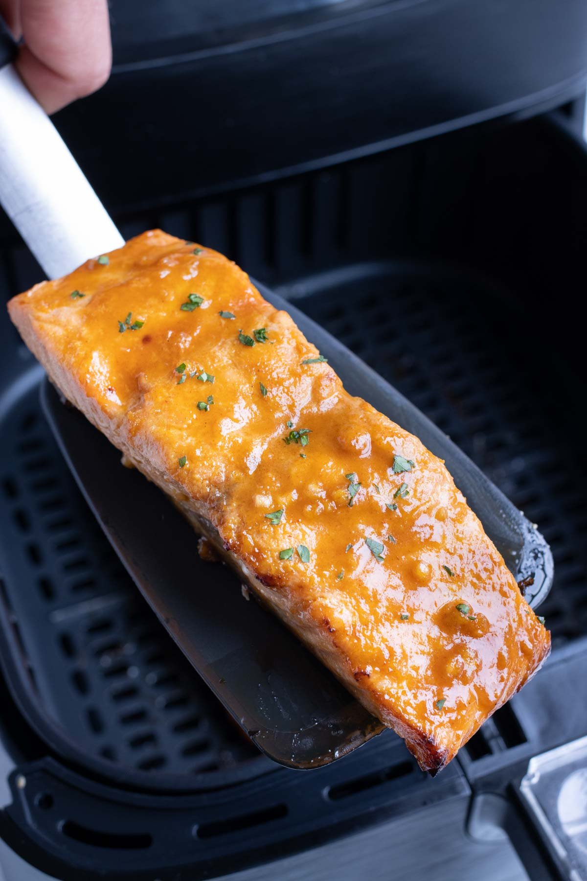 A piece of reheated salmon being taken out of the air fryer with a spatula.