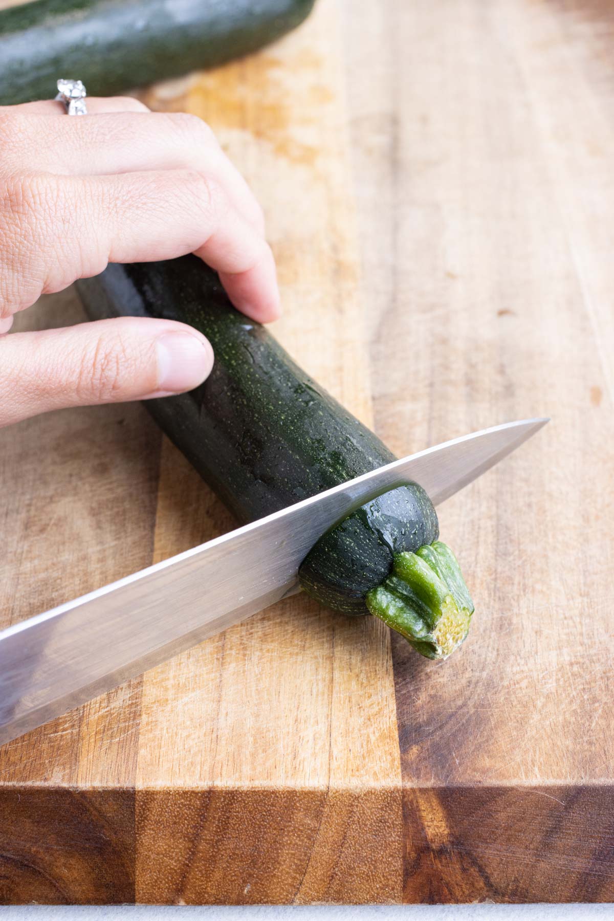A sharp knife slices the end of a zucchini on a cutting board.