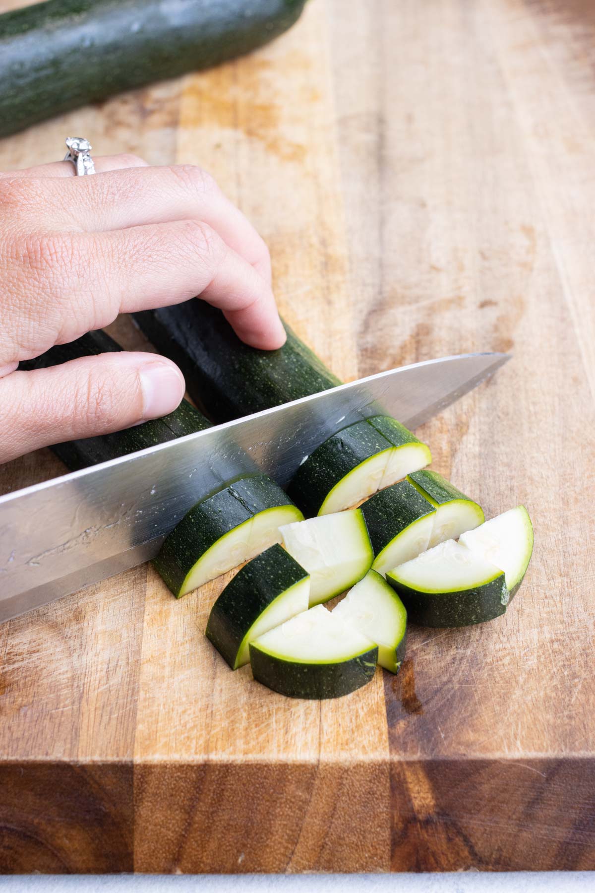 Showing how to slice a zucchini into pieces on a wooden cutting board.