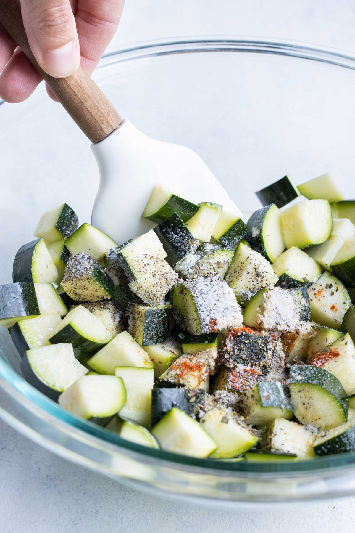 Salt, pepper, and seasonings sprinkled onto sliced zucchini.