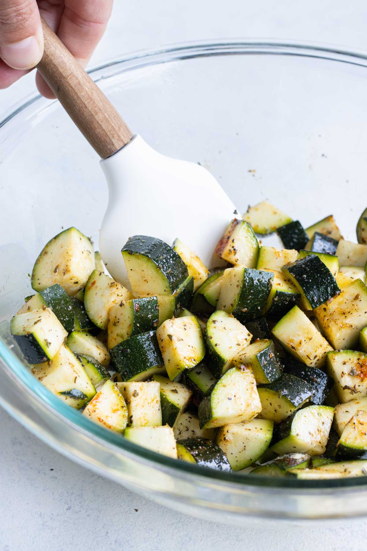 A spatula stirs seasoning zucchini pieces before air frying.
