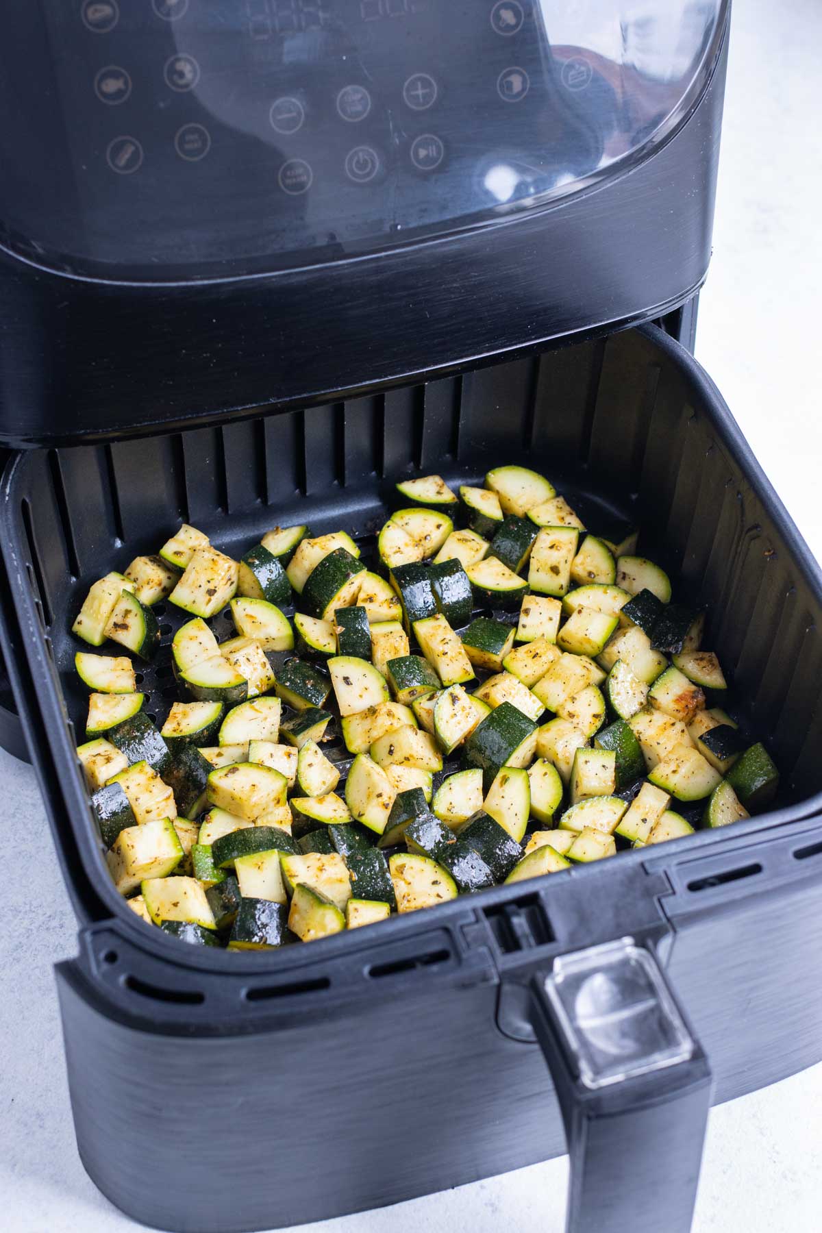 An air fryer basket with a single layer of zucchini pieces.