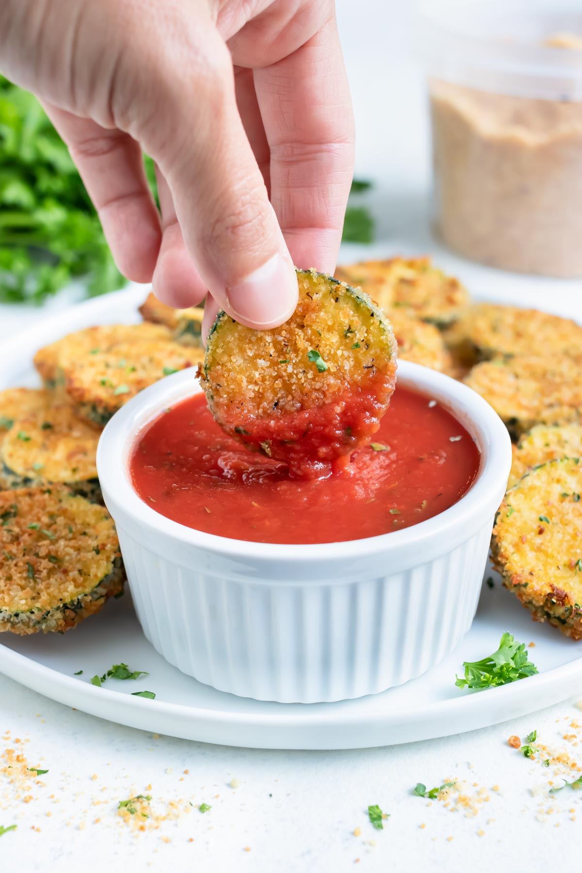 Air Fryer zucchini chips are dipped into a cup of marinara sauce.