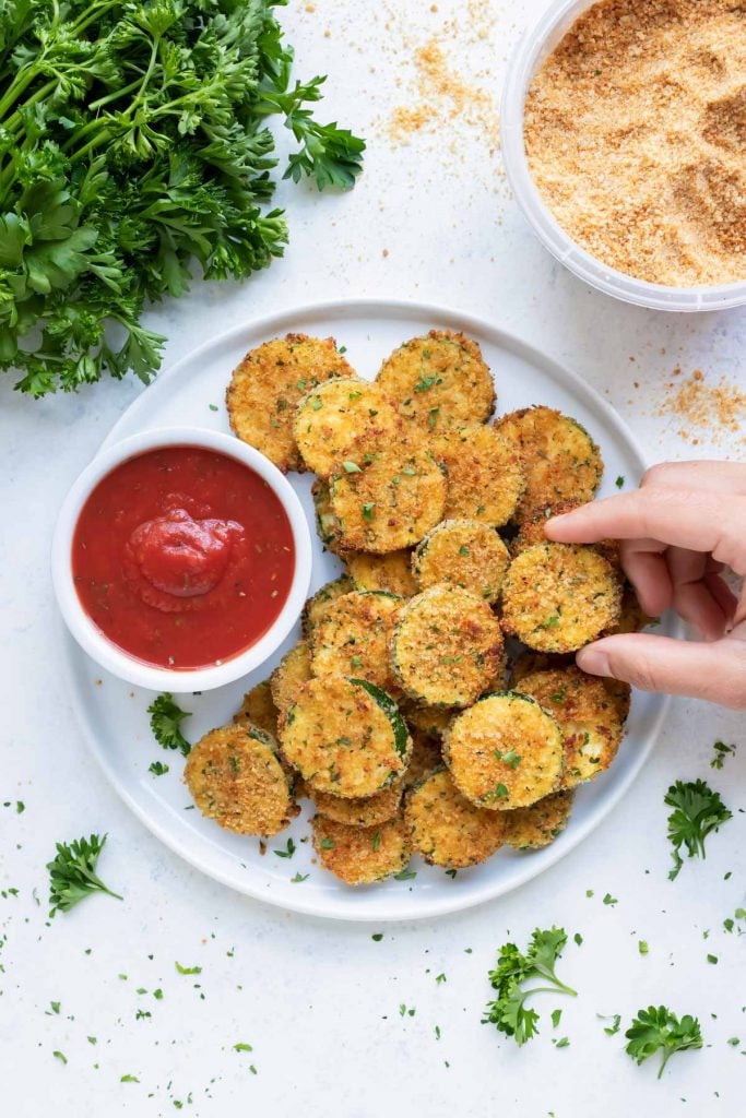 A hand lifting a golden Parmesan zucchini chip.