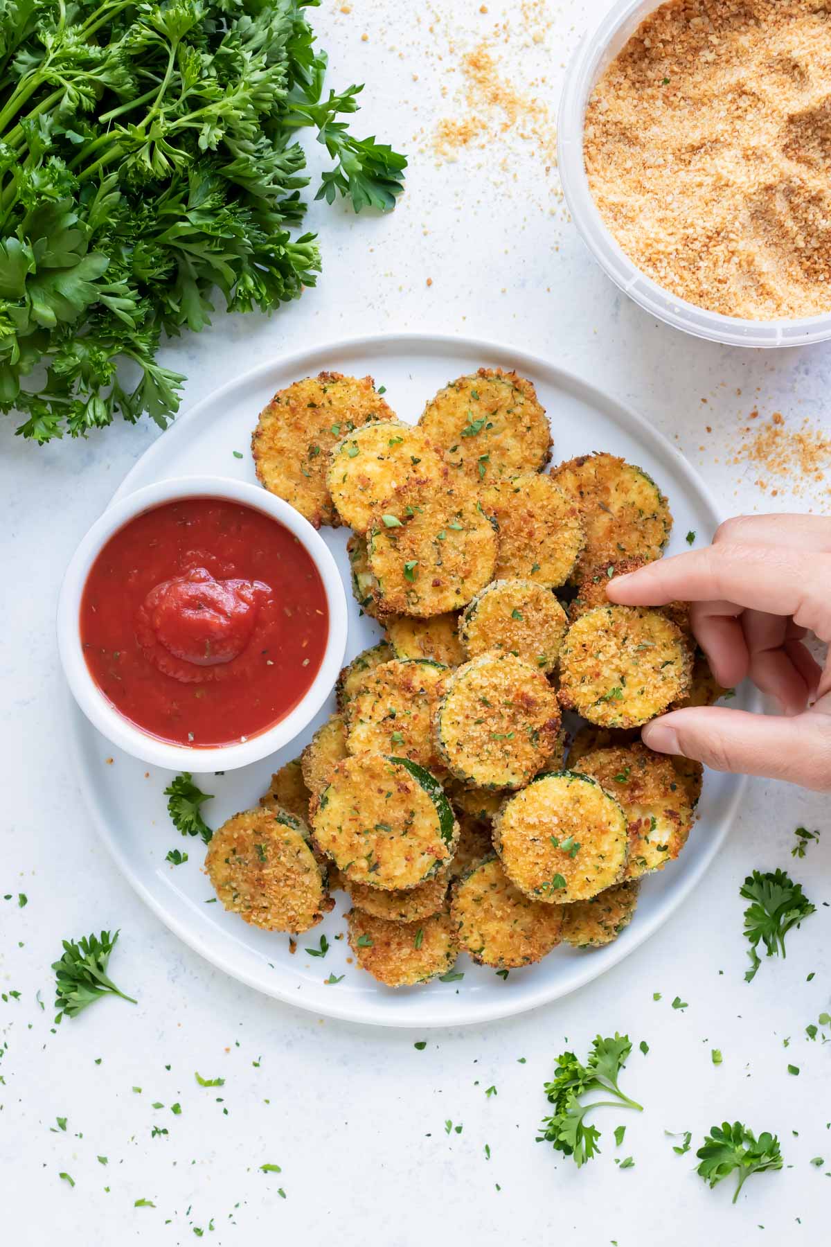 Zucchini chips are lifted up by a hand for a healthy fried appetizer.