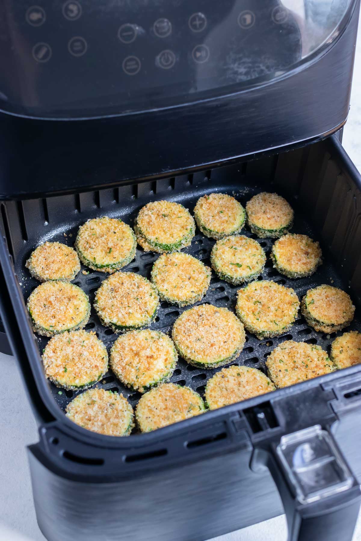 The covered zucchini chips are laid in a flat layer in the air fryer.