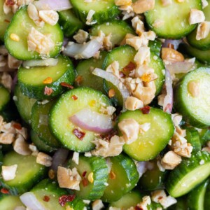 A close up shot of cucumbers with onions, cashews, and dressing.