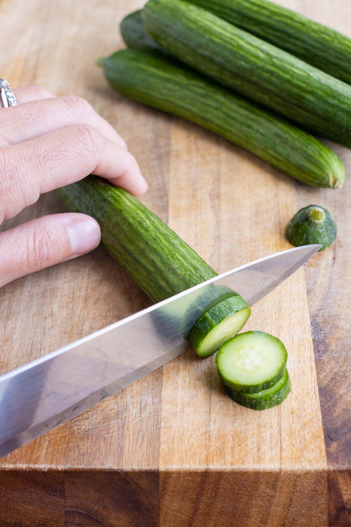 A cucumber is sliced into ¼ inch thick slices on a wooden cutting board.