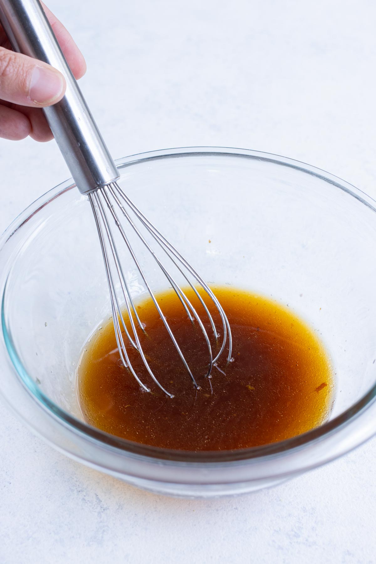 A whisk is used to stir dressing ingredients in a glass bowl.