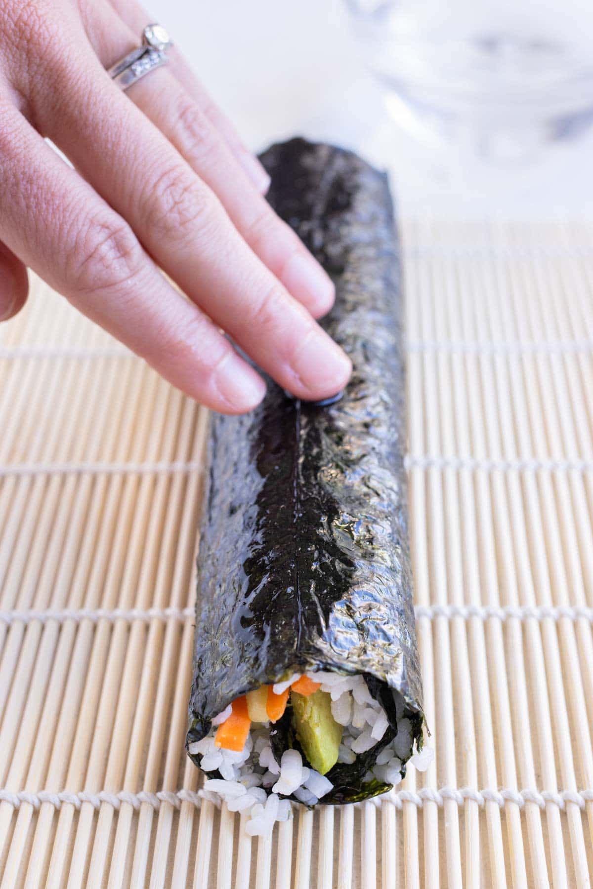 A hand is used to hold the sushi roll before cutting it.