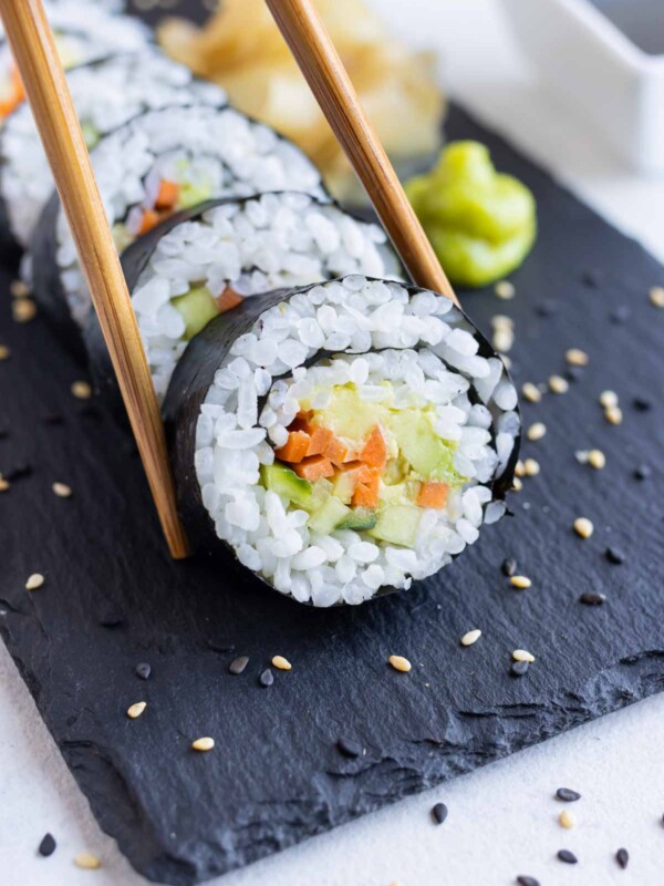 A piece of avocado sushi roll is eaten with chopsticks.