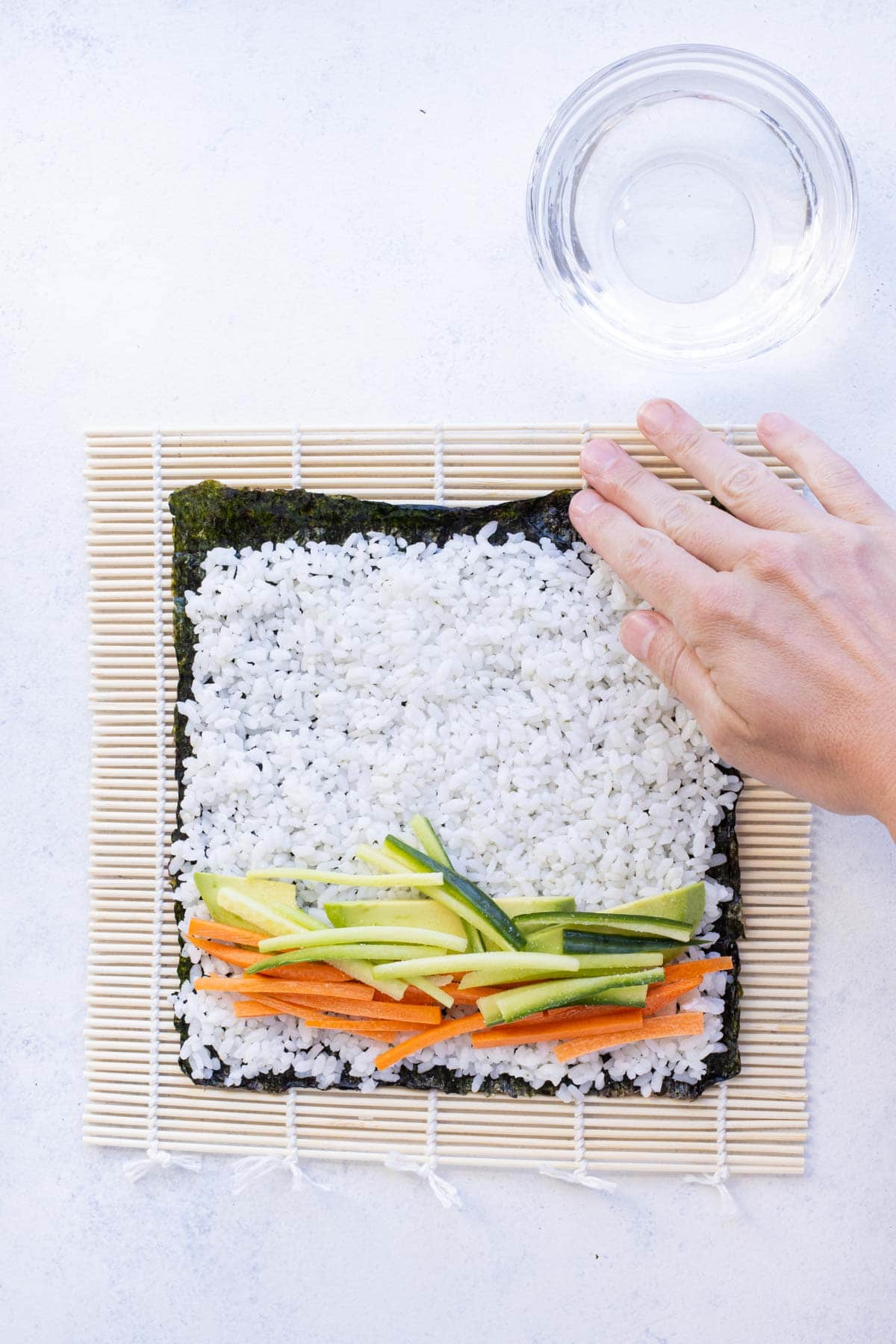 A hand is used to wet the edge of the nori roll.