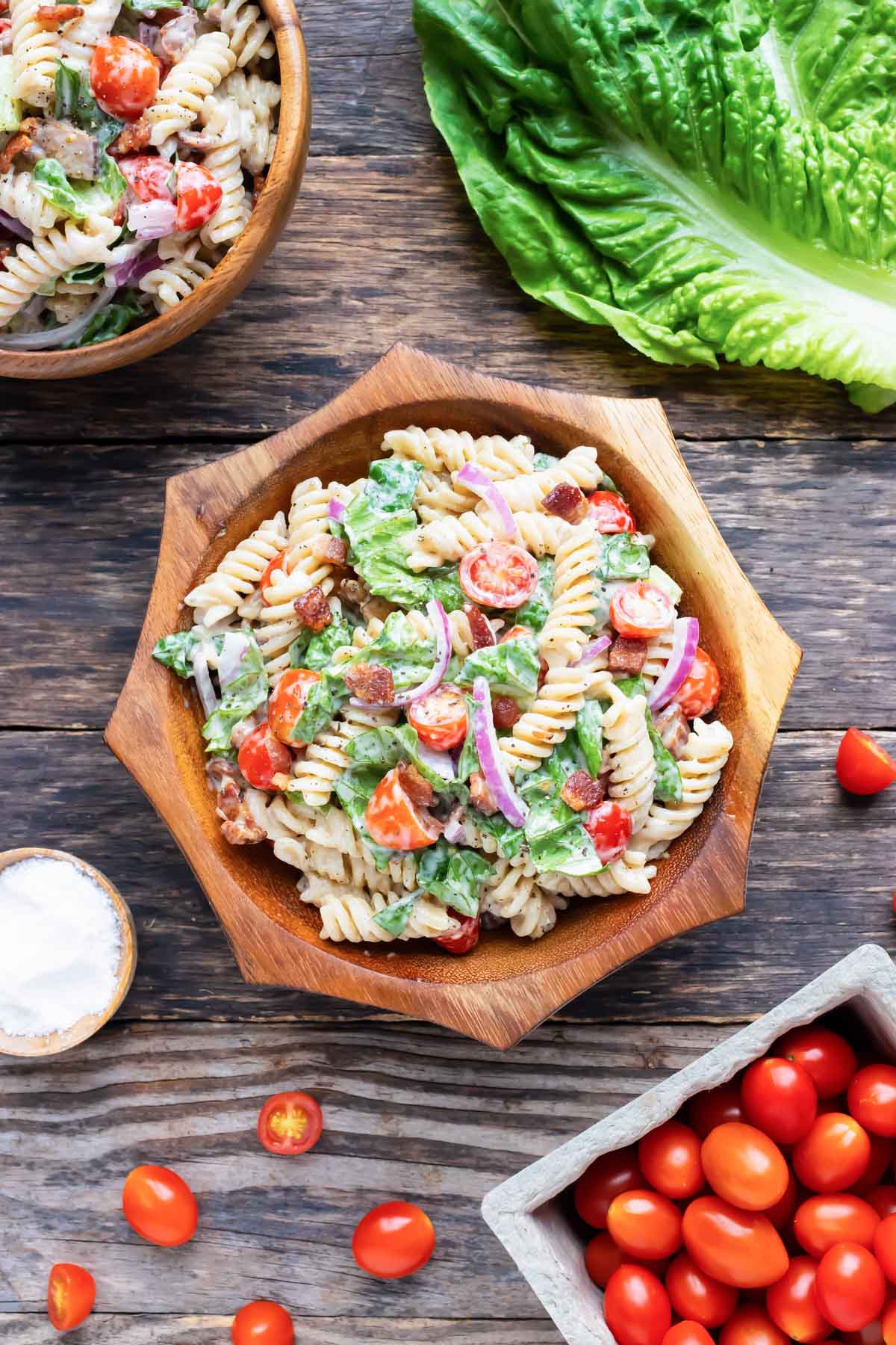 Pasta salad with bacon, tomatoes, and Ranch dressing in a wooden bowl next to Romaine lettuce.