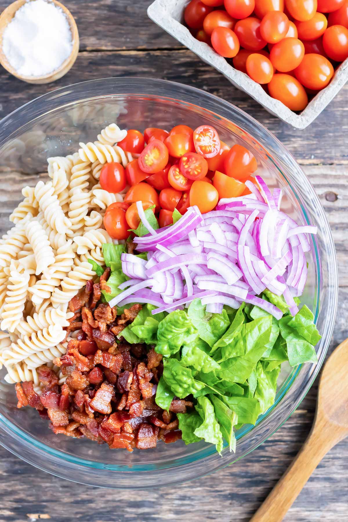 BLT pasta salad recipe next to a wooden spoon and a pint of cherry tomatoes.