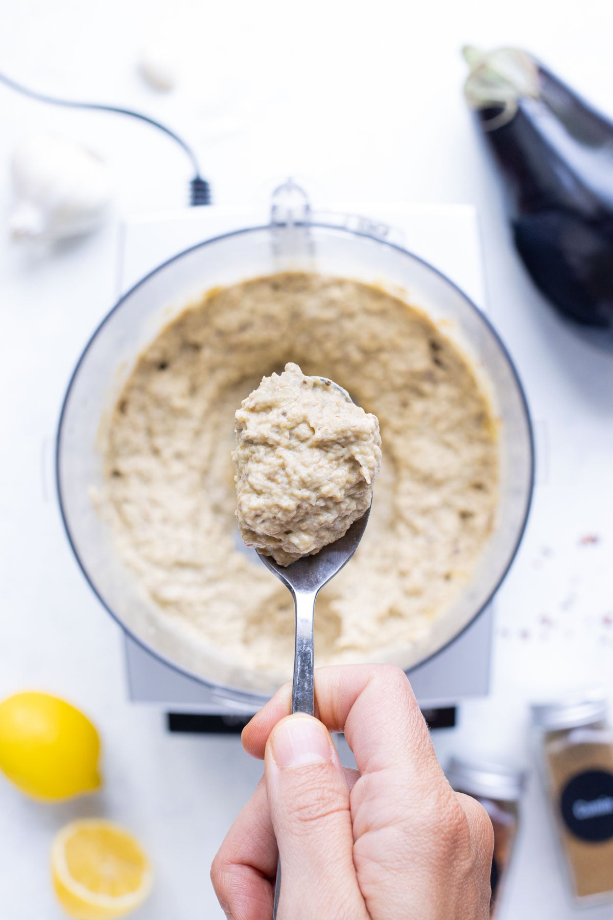 A spoon lifting a scoop of creamy baba ghanoush from the food processor.