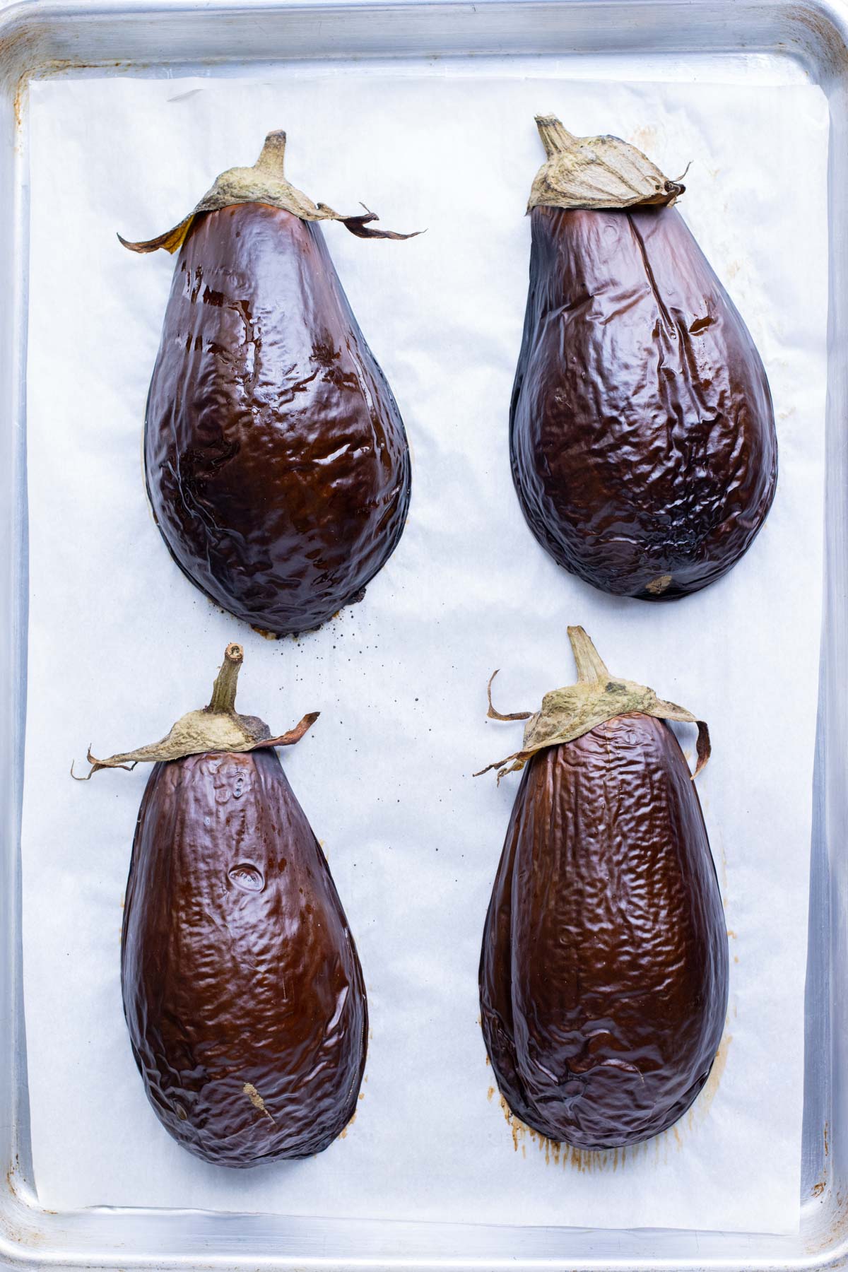 Four eggplant halves are flesh-side down on a baking sheet.