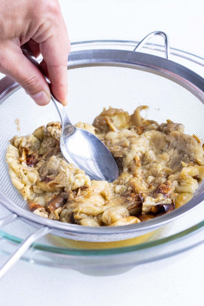 A spoon presses on the eggplant to remove extra moisture.